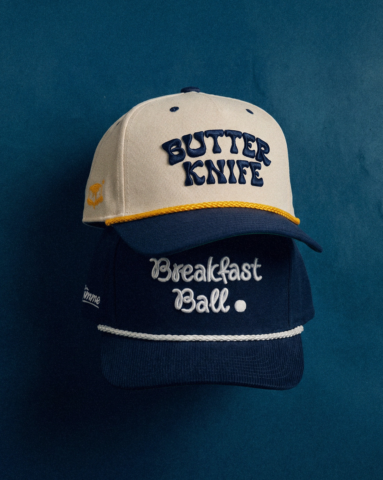 Two baseball caps with 'Butter Knife' and 'Breakfast Ball' text on a blue background