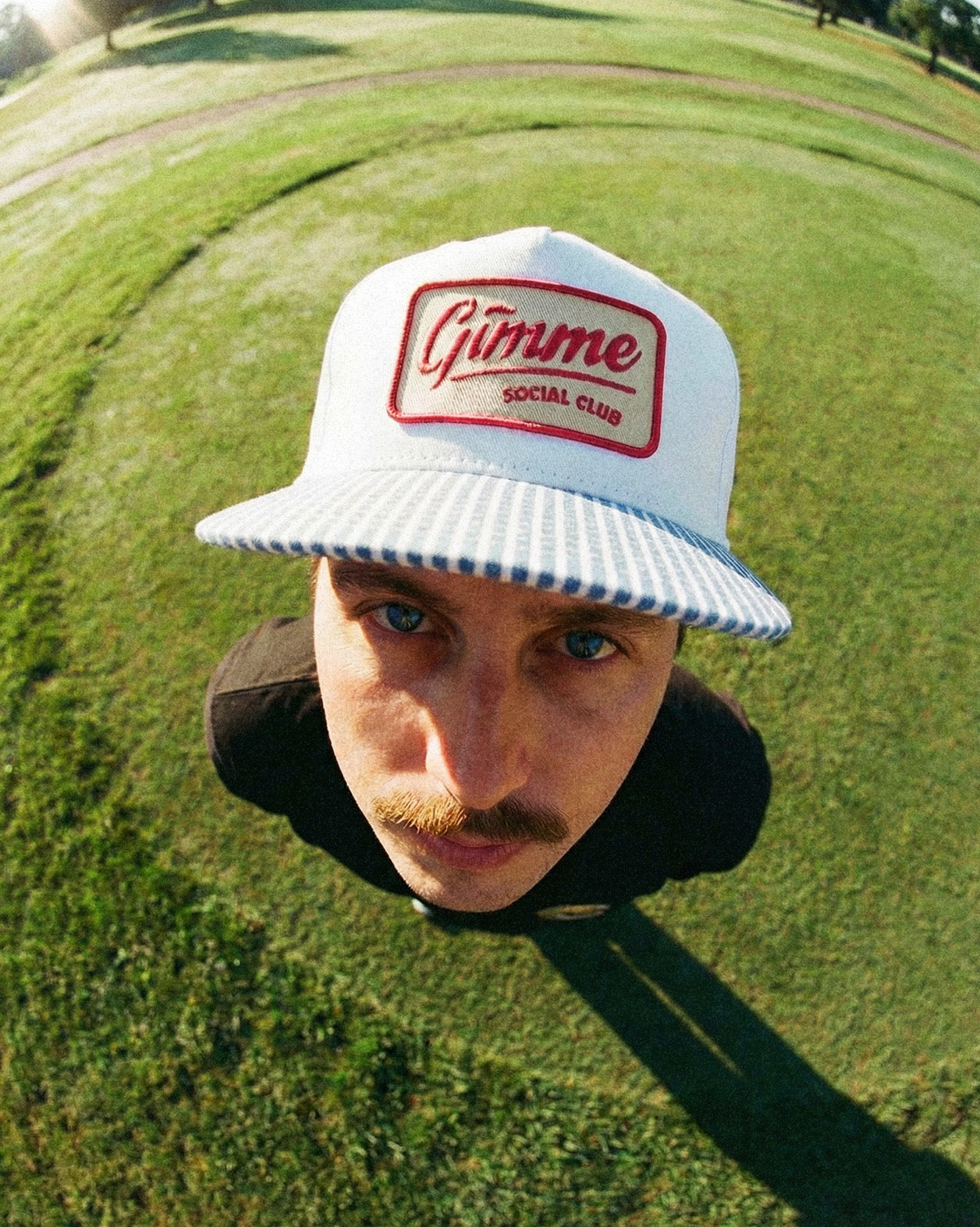 Person wearing a white cap with 'Gimme Social Club' logo on a golf course
